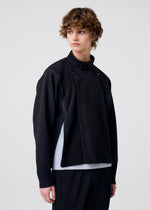 A person with wavy brown hair models the MULTI-FASTENED pleated black long-sleeve top and matching pants by HOMME PLISSÉ ISSEY MIYAKE, styled over a white shirt against a plain light background, gazing off to the side.