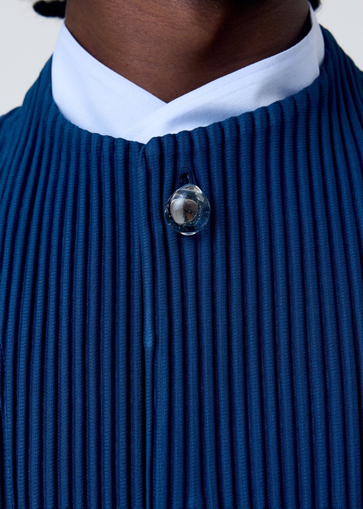 Close-up of a person wearing the HOMME PLISSÉ ISSEY MIYAKE TAILORED PLEATS 1—a deep blue, quick-drying polyester piece with pleats, a white collar, and round clear neckline button. Only the lower face and upper chest are visible. Versatile for any occasion. view 6 of 6