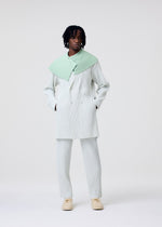 A person stands against a plain white background wearing the HOMME PLISSÉ ISSEY MIYAKE TAILORED PLEATS 3 light blue pinstriped double-breasted jacket, a mint green textured scarf, beige shoes, and has short dreadlocks.