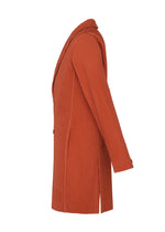 The TAILORED PLEATS 3 coat by HOMME PLISSÉ ISSEY MIYAKE is a rust-colored, long-sleeved, knee-length polyester piece with a notched collar and vertical ribbed texture, shown in side profile against a white background.