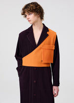 A person with curly brown hair models the HOMME PLISSÉ ISSEY MIYAKE PAINTER’S GEAR: a long, dark pinstriped coat with a bold orange textured one-shoulder vest-style panel and pocket, set against a plain light background.