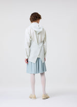 A person with short curly hair models HOMME PLISSÉ ISSEY MIYAKE's MONTHLY COLORS : JUNE, featuring lightweight pleated skirt-style shorts, white tights, cream shoes, and a unique structured white top with crossed pleats, on a plain white background.