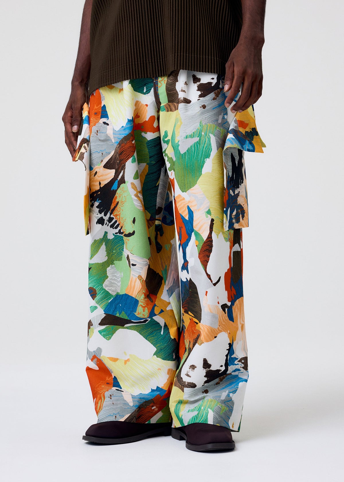 Wearing PALETTE MARBLED wide pants by HOMME PLISSÉ ISSEY MIYAKE, featuring a vibrant abstract marbled pattern in green, orange, yellow, blue, and black; the person stands against a plain background in dark sandals with a brown top partly visible. view 6 of 6