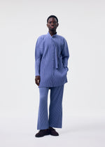 A person stands against a plain light background, wearing the HOMME PLISSÉ ISSEY MIYAKE MONTHLY COLORS : FEBRUARY set—long, loose-fitting blue pinstriped shirt and matching wide-leg trousers—with dark shoes, one hand in their pocket and a neutral expression.