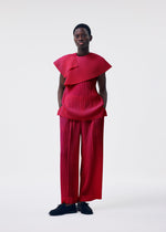 A person wears the MONTHLY COLORS : JANUARY set from HOMME PLISSÉ ISSEY MIYAKE—bold, structured red pleated wrap top with matching wide-legged pants and black shoes against a plain background.