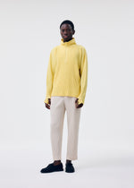 A person wearing the MONTHLY COLORS : MARCH yellow polyester long-sleeve top by HOMME PLISSÉ ISSEY MIYAKE, paired with cream pants and black shoes, stands against a white background, looking directly at the camera with a neutral expression.