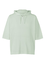 The MONTHLY COLORS : JUNE by HOMME PLISSÉ ISSEY MIYAKE is a lightweight, light green hooded pullover featuring short sleeves, ribbed texture, a front pocket, drawstrings, and a single button at the collar. - BOBOLI MOSS ASH （no.70）