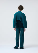 A person with curly hair stands facing away against a plain light background, wearing a teal HOMME PLISSÉ ISSEY MIYAKE COLOR PLEATS 1 pleated jersey top with wide sleeves, matching pants, and black shoes.