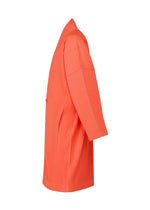 Side view of the MONTHLY COLORS : APRIL coat by HOMME PLISSÉ ISSEY MIYAKE: a bright orange, knee-length, kimono-style coat with ribbed texture, relaxed fit, single-breasted front, two pockets, and quick-drying polyester.