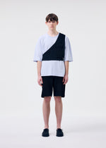 A person stands against a plain white background wearing HOMME PLISSÉ ISSEY MIYAKE RUSTIC KNIT black shorts, a loose white T-shirt with a black diagonal accent, and black shoes, facing forward with a neutral expression.