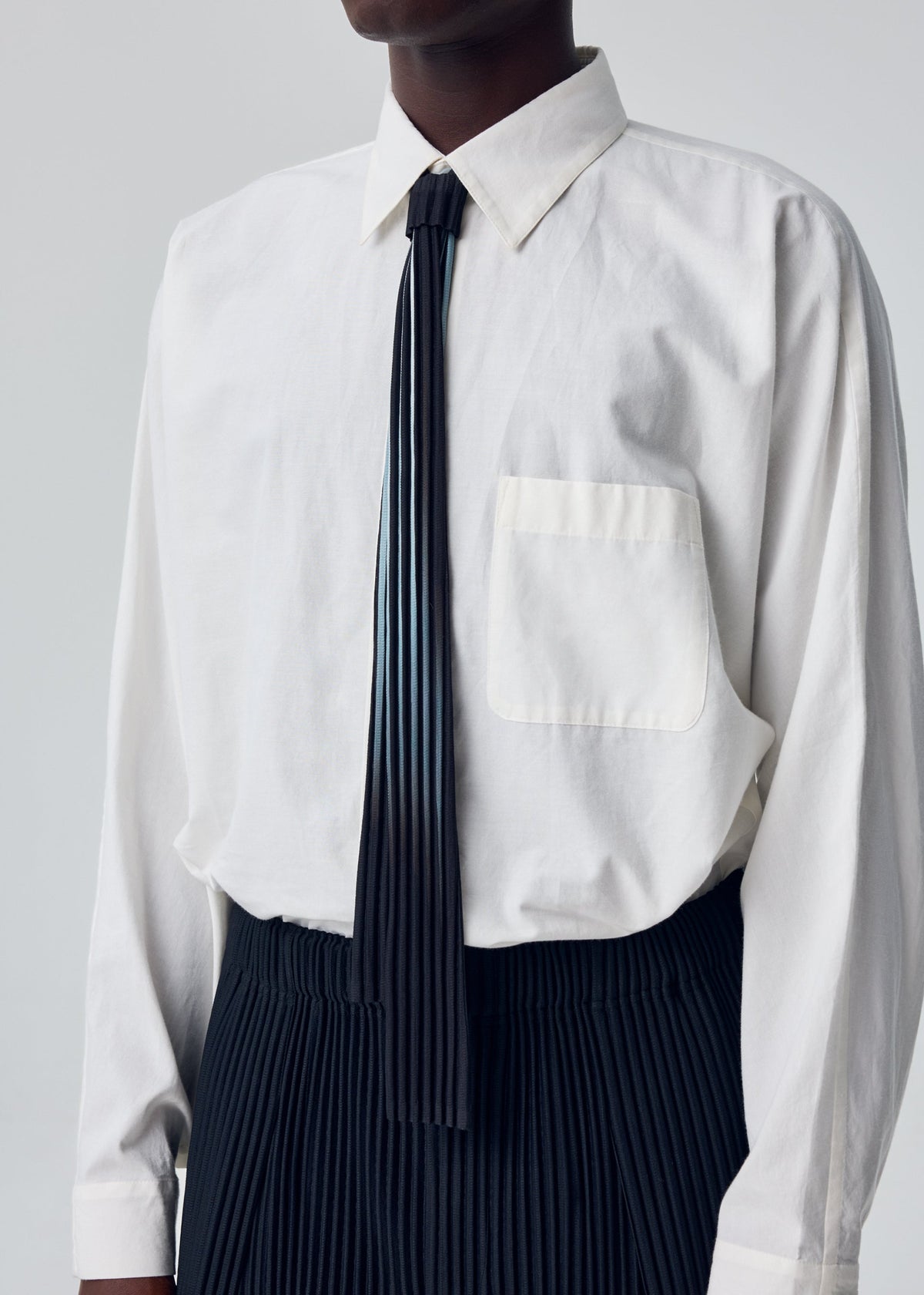 A person wears a white button-up shirt, black pleated pants, and the IN THE SHADOW PLEATS TIE by HOMME PLISSÉ ISSEY MIYAKE—cropped from chest to mid-thigh against a plain background. view 4 of 4