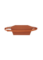 The PLEATS SLIM BAG by HOMME PLISSÉ ISSEY MIYAKE is a flat, rectangular shoulder bag in rust color, featuring a ribbed texture, an adjustable strap, and a lightweight design, shown against a white background.