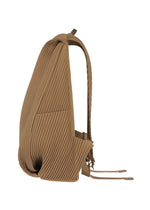 A side view of the tan PLEATS BACKPACK by HOMME PLISSÉ ISSEY MIYAKE, featuring pleats, side pockets, and thin shoulder straps, shown against a white background.