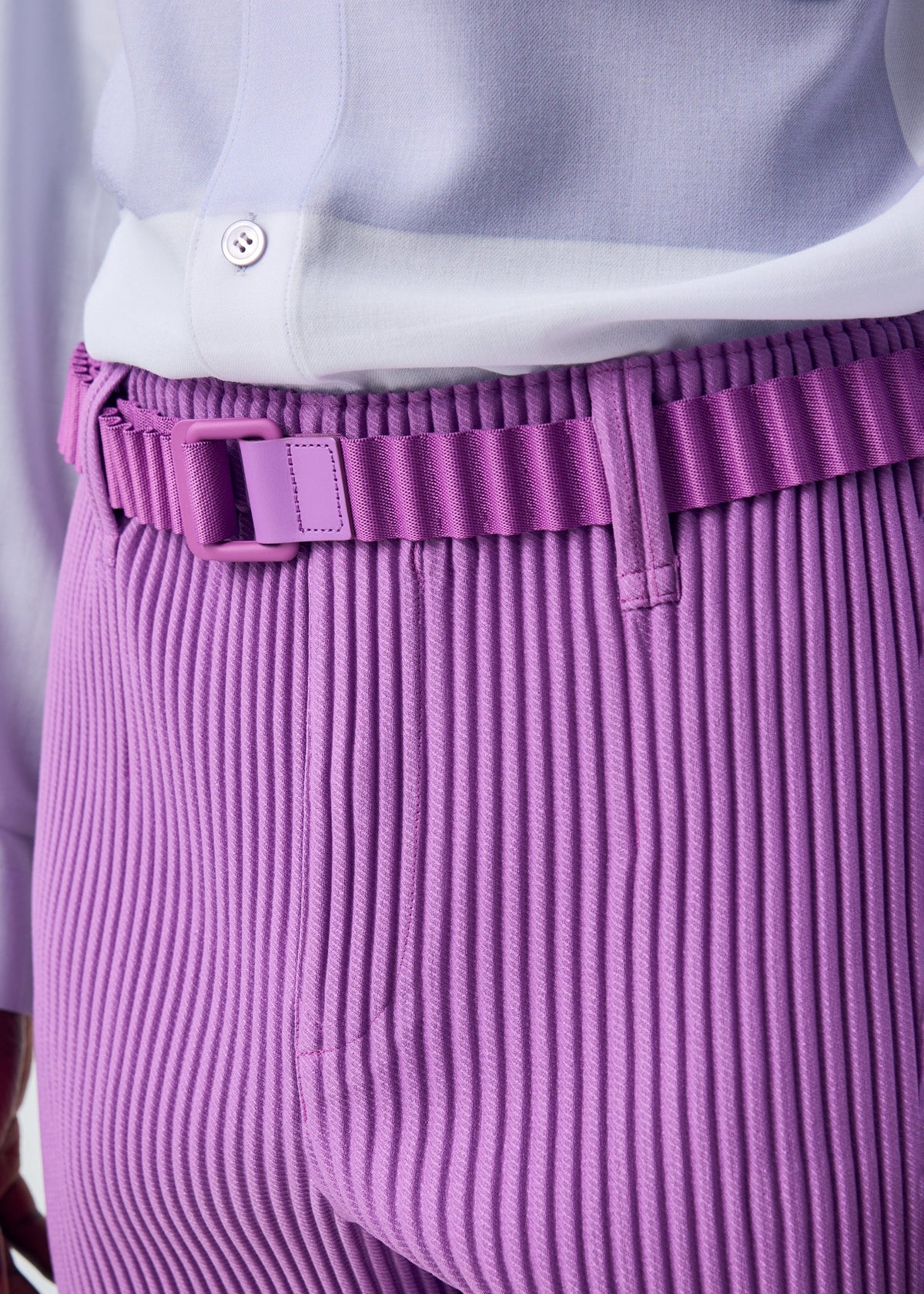 Close-up of a person wearing the HOMME PLISSÉ ISSEY MIYAKE PLEATS BELT in lavender, paired with pleated pants and a tucked-in white shirt. view 6 of 6