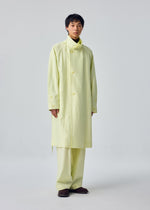 A person stands facing forward in the OPACITY pale yellow long hooded coat and matching pants by HOMME PLISSÉ ISSEY MIYAKE, crafted from a nylon linen blend, paired with dark shoes against a plain light-colored background.