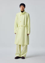 A person is wearing the OPACITY light yellow belted trench coat with a detachable hood and matching wide-leg pants from HOMME PLISSÉ ISSEY MIYAKE, styled with dark shoes and posed against a plain light background.