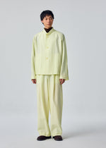 A person stands facing forward, dressed in the OPACITY jacket and matching wide pants from HOMME PLISSÉ ISSEY MIYAKE—a loose-fitting, pale yellow linen-blend ensemble—paired with dark shoes against a plain light background.