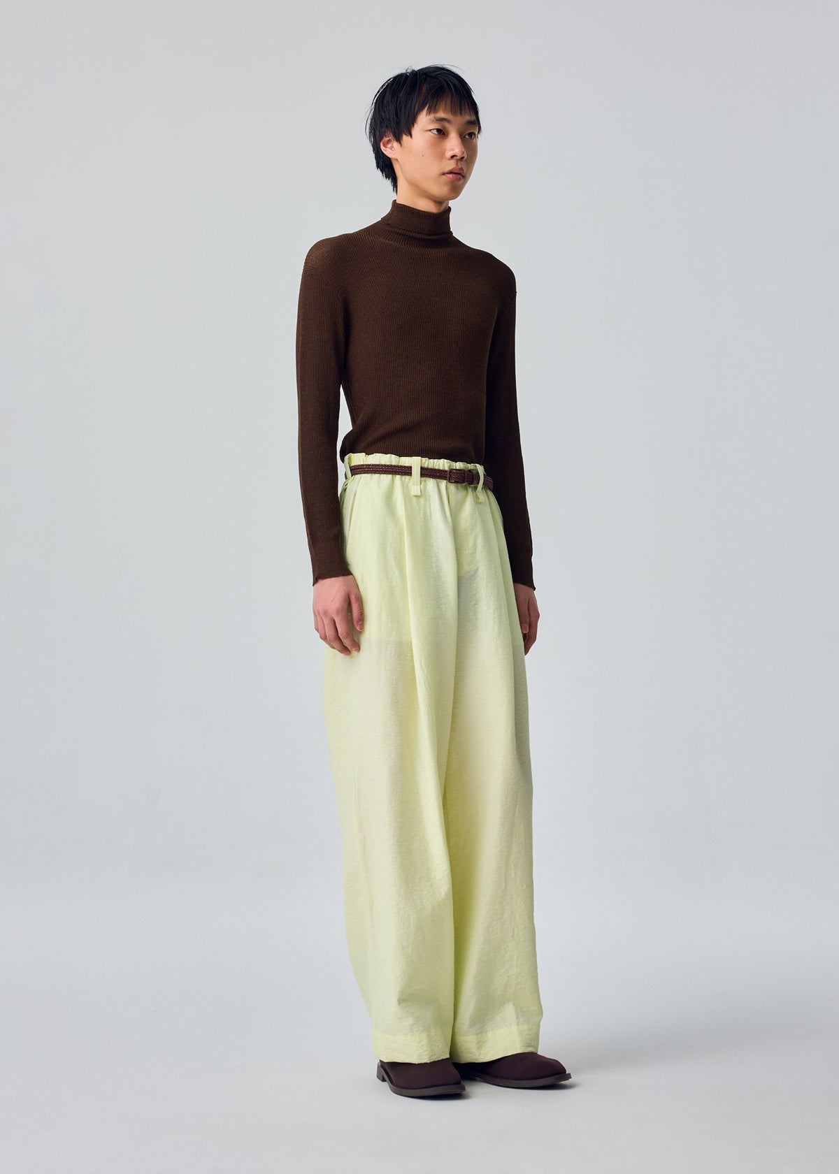 An individual stands against a plain light gray background, dressed in the OPACITY turtleneck by HOMME PLISSÉ ISSEY MIYAKE paired with cream linen blend wide-leg pants and brown shoes. view 6 of 8