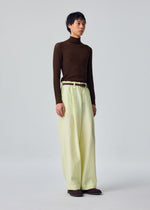 An individual stands against a plain light gray background, dressed in the OPACITY turtleneck by HOMME PLISSÉ ISSEY MIYAKE paired with cream linen blend wide-leg pants and brown shoes.