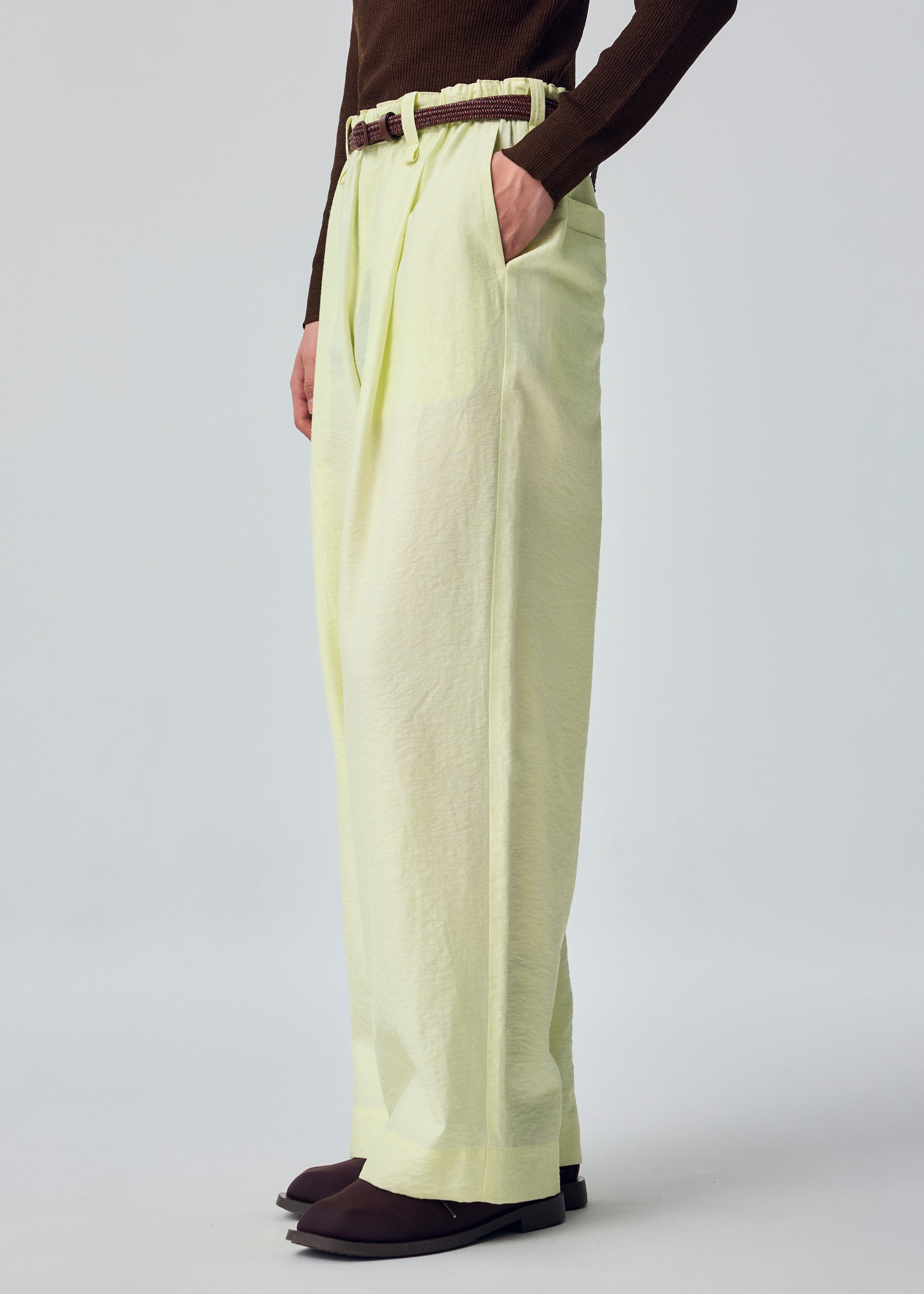 Zoomed view A person stands with one hand in their pocket against a plain background, wearing the OPACITY light yellow linen-blend wide-leg pants from HOMME PLISSÉ ISSEY MIYAKE, styled with a brown belt, a dark brown long-sleeve top, and dark shoes.
