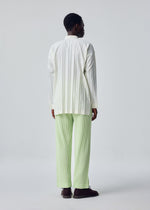 A person with short hair stands against a plain light background, wearing the HOMME PLISSÉ ISSEY MIYAKE EDGE SHIRT with hand pleating and relaxed-fit light green pleated pants, finished with dark shoes.