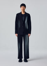 A person stands facing forward wearing the IN THE SHADOW jacket by HOMME PLISSÉ ISSEY MIYAKE, paired with a black shirt and shoes, against a plain light gray background.