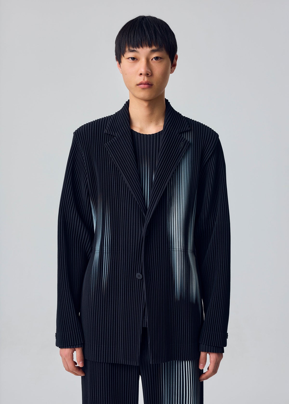 A person with short black hair wears the IN THE SHADOW set by HOMME PLISSÉ ISSEY MIYAKE—loose-fitting, optical-illusion stripe jacket and pants—against a plain light gray background. view 6 of 6