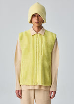 A person in the HOMME PLISSÉ ISSEY MIYAKE FLEECE PLEATS vest, matching hat, and beige pleated shirt and pants stands facing the camera against a plain light background.