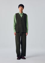 A person stands facing forward, wearing the HOMME PLISSÉ ISSEY MIYAKE SLASH set: a light green collared shirt underneath a dark green, front-opening pinstriped vest and matching pinstriped pants with slash pockets, paired with brown shoes, against a plain light background.