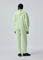 A person faces away, wearing HOMME PLISSÉ ISSEY MIYAKE’s MONTHLY COLORS : JULY light green ribbed hoodie and matching straight pants with a drawcord waist, paired with dark shoes, set against a plain light gray background.