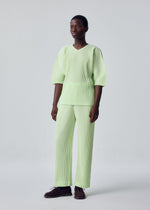 A person with short hair wears the HOMME PLISSÉ ISSEY MIYAKE MONTHLY COLORS: JULY set—pastel green, ribbed, loose-fitting top with elbow-length sleeves and matching straight pants in quick-drying polyester—paired with dark shoes.