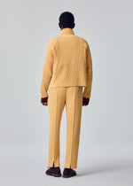 A person stands facing away, wearing the HOMME PLISSÉ ISSEY MIYAKE TAILORED PLEATS 1 set in yellow—comprising a ribbed jacket and center-pressed pants—with brown shoes, against a plain light gray background.