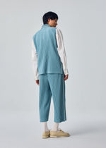 A person stands facing away against a plain light gray background, wearing the HOMME PLISSÉ ISSEY MIYAKE EMBROIDERY STRIPES pleated cropped pants and vest set in light blue, paired with a long-sleeve white shirt, white socks, and beige shoes.