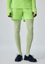 Wearing the COLOR PLEATS 1 set by HOMME PLISSÉ ISSEY MIYAKE, this person sports a neon green ribbed long-sleeve top and matching vibrant sporty shorts, paired with light green ribbed tights and black lace-up shoes, standing against a plain light background.