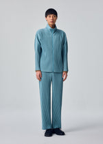 A person stands against a plain background wearing the COLOR PLEATS 2 set from HOMME PLISSÉ ISSEY MIYAKE—a matching light blue pleated jacket and sporty straight pants crafted from quick-drying polyester—paired with black shoes, looking straight ahead with a neutral expression.