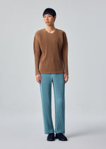 A person stands against a plain background, wearing the HOMME PLISSÉ ISSEY MIYAKE COLOR PLEATS 2 long-sleeved pleated top in brown and light blue sporty straight pants with a drawcord waist, paired with black shoes.
