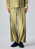 A person wears HOMME PLISSÉ ISSEY MIYAKE's BLEND OF LIGHTS yellow pants with black vertical stripes, pleats, and drawcord waist, a matching top partially visible, and black shoes against a plain light background.