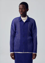 A person wears the HOMME PLISSÉ ISSEY MIYAKE RUSTIC MESH long-sleeved blue button-up shirt over a cream turtleneck, standing against a plain light gray background and looking slightly to the side.