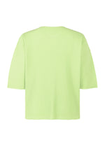 The HOMME PLISSÉ ISSEY MIYAKE MONTHLY COLORS : JULY top is shown in light green with short sleeves, ribbed V-neck, and vertical textured lines. The loose, lightweight fit is highlighted against a white background with the back view visible.