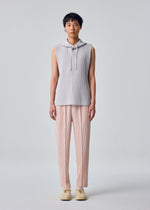 A person stands facing forward against a plain light gray background, wearing the HOMME PLISSÉ ISSEY MIYAKE MONTHLY COLORS : SEPTEMBER sleeveless hoodie in light gray—a lightweight, quick-drying polyester style—paired with loose, pale pink pleated pants and cream-colored shoes.