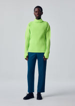 A person stands against a plain background wearing a bright green sporty long-sleeved ribbed turtleneck sweater with thumbhole sleeves, blue COLOR PLEATS 1 trousers by HOMME PLISSÉ ISSEY MIYAKE, and black shoes.