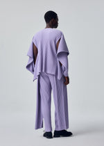 A person faces away, wearing HOMME PLISSÉ ISSEY MIYAKE's MOTION BLUR—a loose, pleated jersey top with wide sleeves and matching pants. The plain light background highlights its modern texture and versatile styling options.