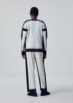 A person faces away, wearing the FRAMEWORK : CHUSEN top by HOMME PLISSÉ ISSEY MIYAKE—white, pleated, long-sleeved with black trim—paired with black shoes against a plain light background.