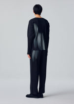 A person with short dark hair wears the IN THE SHADOW set by HOMME PLISSÉ ISSEY MIYAKE—loose, optical-illusion stripe top and matching wide-leg pinstriped pants—with black shoes, against a light gray background.