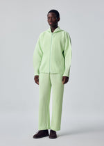 A person stands facing forward in HOMME PLISSÉ ISSEY MIYAKE's MONTHLY COLORS : JULY—light green, quick-drying polyester zip-up hoodie and matching wide-leg pants—and dark brown shoes, set against a plain light background.