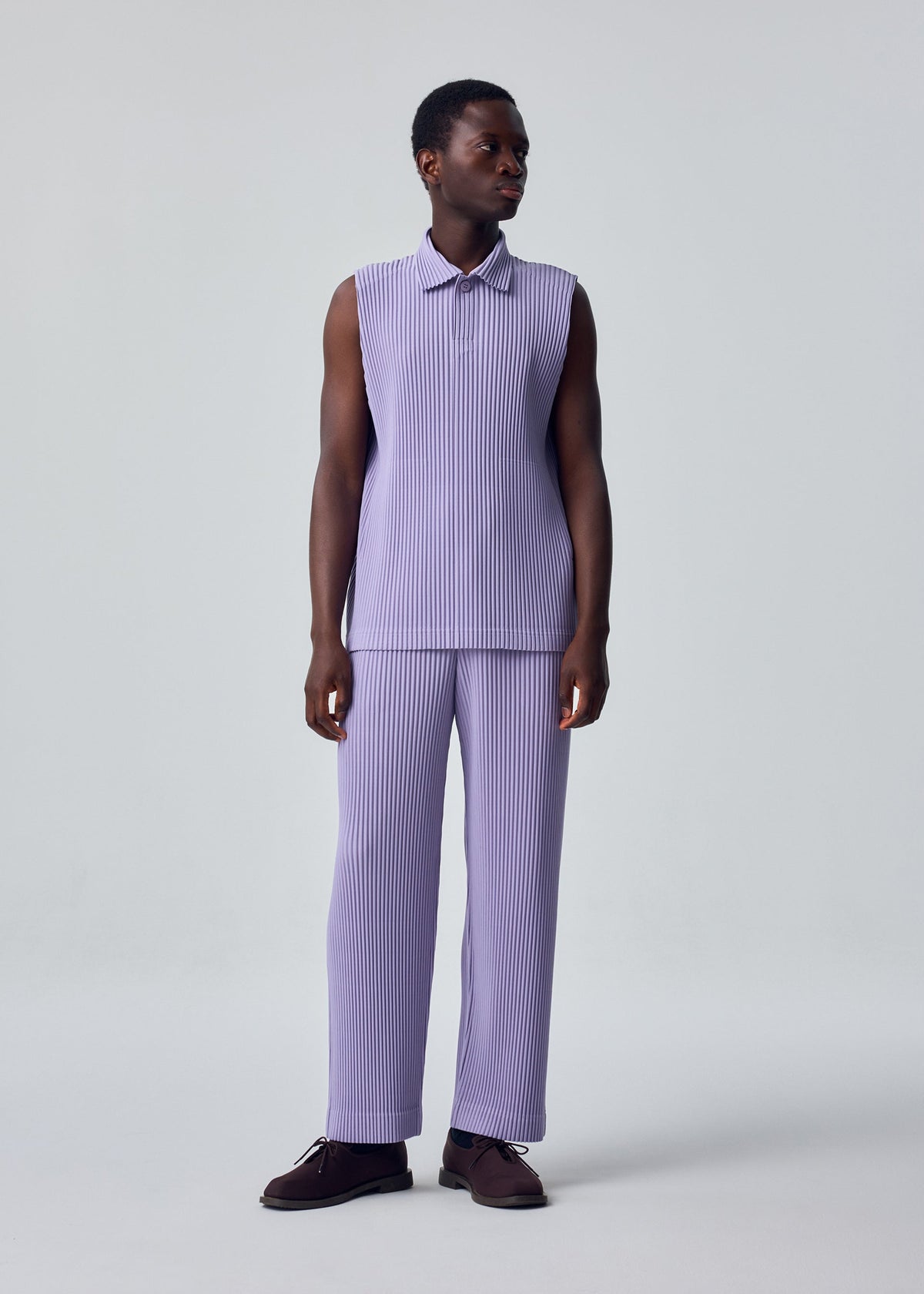 A person stands against a plain light background wearing the MONTHLY COLORS : JULY sleeveless, light purple pleated collared top and matching trousers by HOMME PLISSÉ ISSEY MIYAKE. They have short hair, dark shoes, and look slightly to the side. view 4 of 6