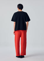 A person stands facing away against a plain light gray background, wearing the HOMME PLISSÉ ISSEY MIYAKE BASIC KNIT black short-sleeve shirt, bright red pleated jersey pants, and black shoes.
