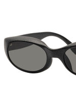 Close-up of the left side of ISSEY MIYAKE EYES GRIT-SQUARE black 3D printed sunglasses with dark oval lenses, shown against a white background.