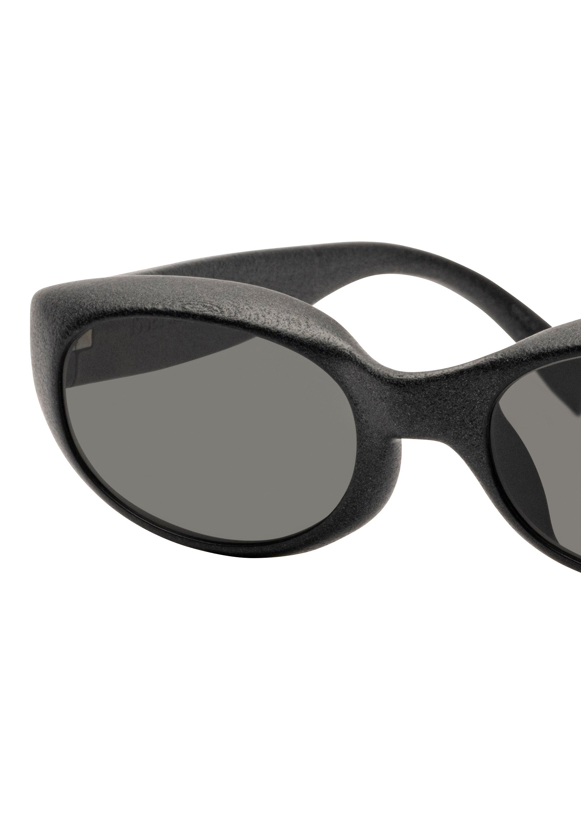 Zoomed view Close-up of the left side of ISSEY MIYAKE EYES GRIT-SQUARE black 3D printed sunglasses with dark oval lenses, shown against a white background.