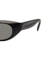 Close-up of the left side of ISSEY MIYAKE EYES GRIT-SQUARE black square sunglasses, highlighting the thick textured arm and the edge of a dark lens set against a white background.